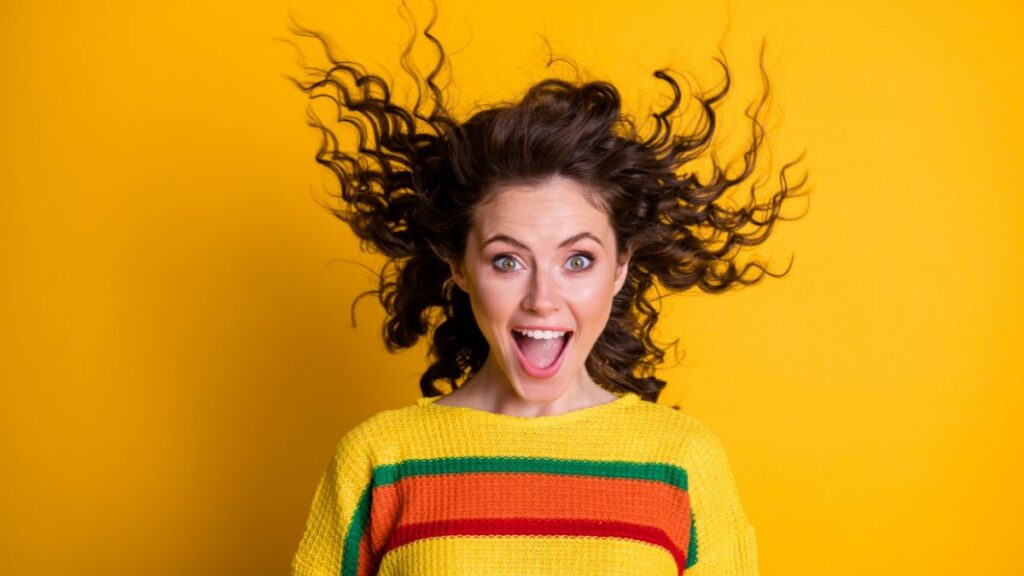 Photo of surprised amazed woman dressed casual colorful sweatshirt wind blowing hair open mouth isolated yellow color background