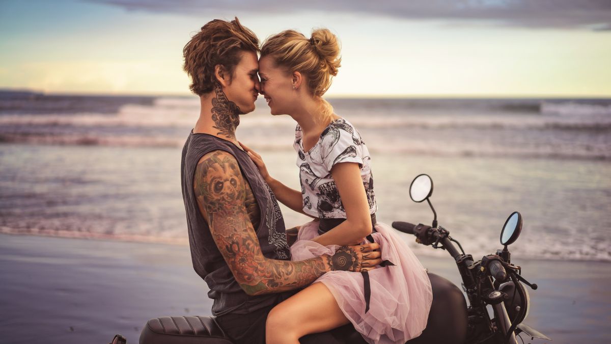 A couple facing each other on a bike in front of the water