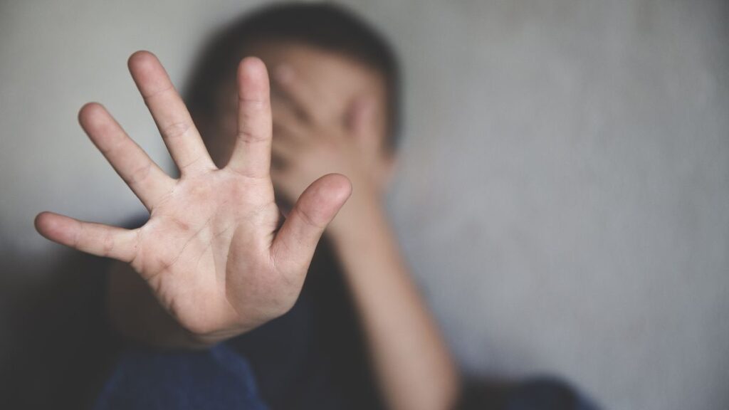 Being a Domestic Violence Victim: blurred man sitting with one hand up and one hand covering his face.