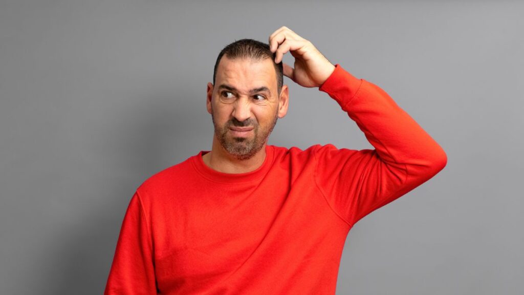 Man wearing a red shirt scratching his head