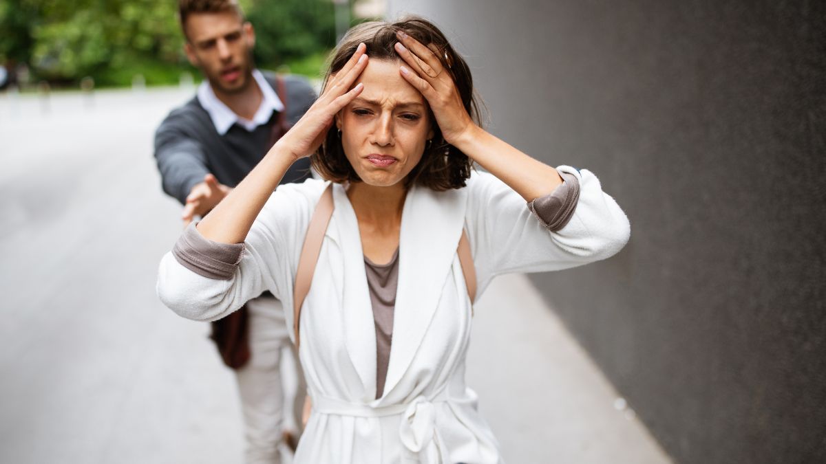 couple arguing, woman looking defeated and holding her head as she walks away -