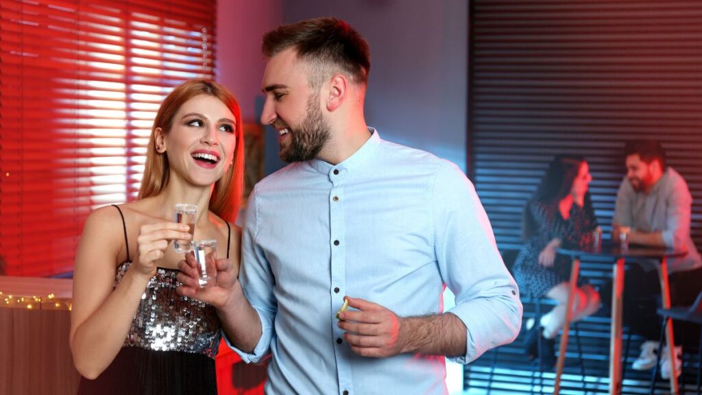 couple at a bar doing cheers with shots