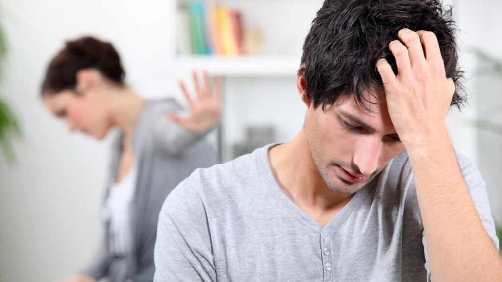 couple sitting apart in a fight man with hand on his head looking down