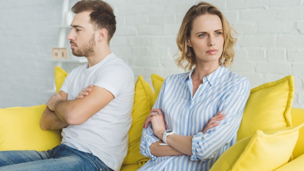 couple sitting on a yellow couch upset looking away from each other