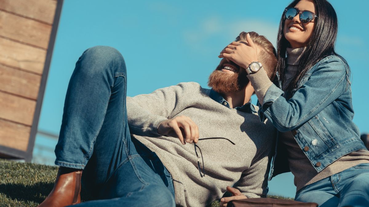 couple sitting on the grass woman covering mans eyes smiling