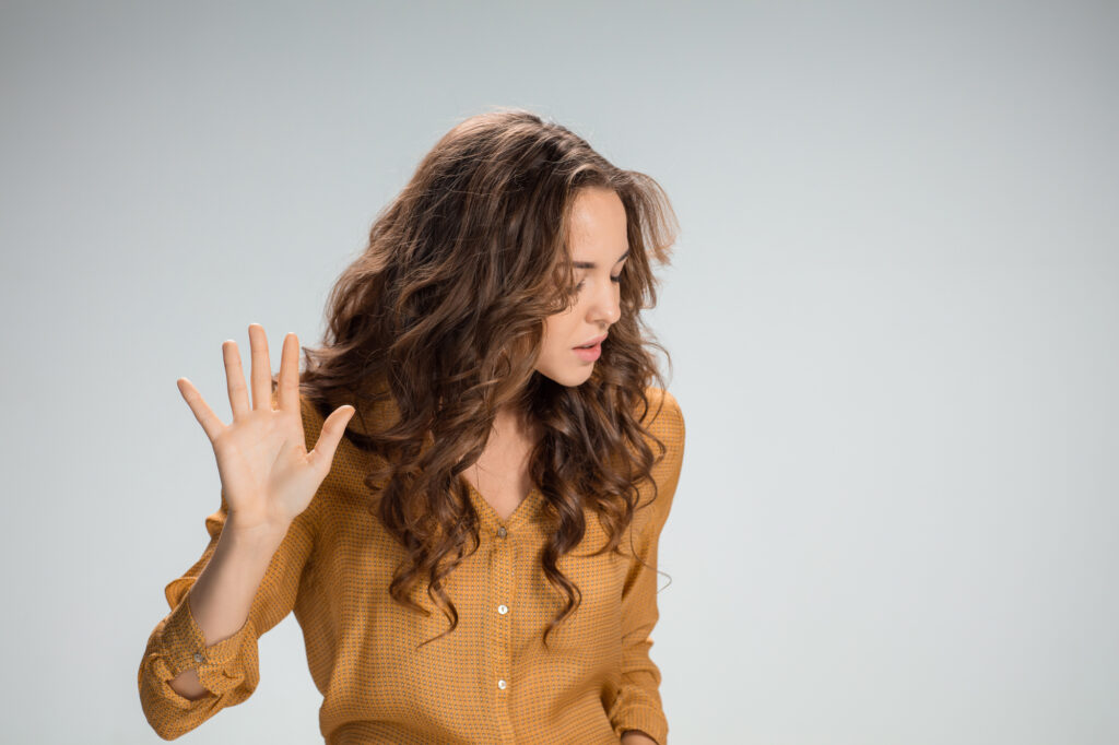 The young woman's portrait with frightened emotions on gray background. She pushing something with hand