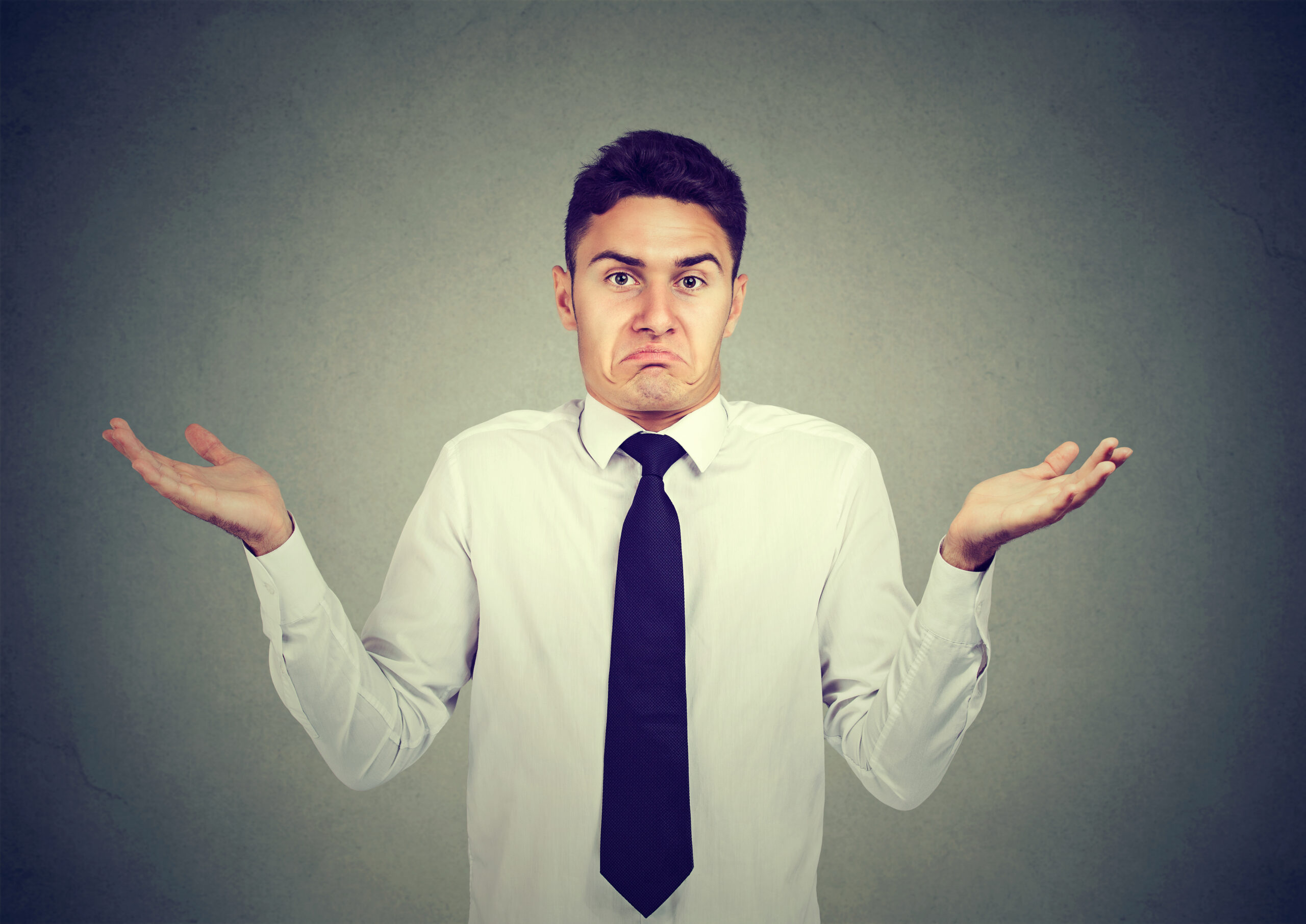 Closeup portrait young business man shrugging shoulders isolated on gray wall background. Body language