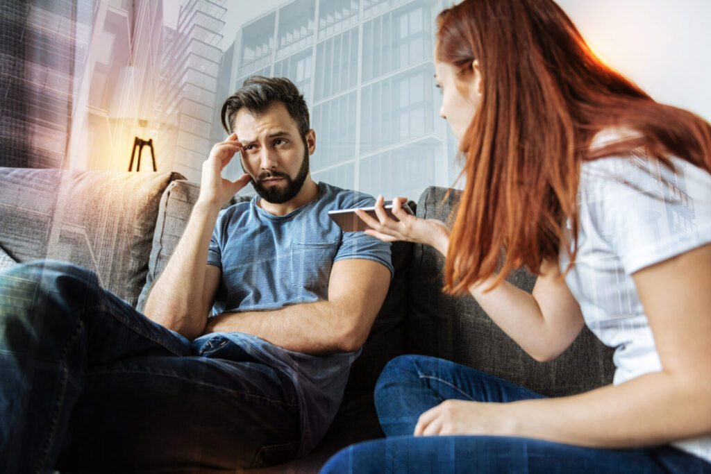 DepoExplain it. Young emotional strict woman feeling jealous and looking at her quiet boyfriend while showing him a smartphone and waiting for his explanations of the last messagessitphotos_187119512_L-1536x1025