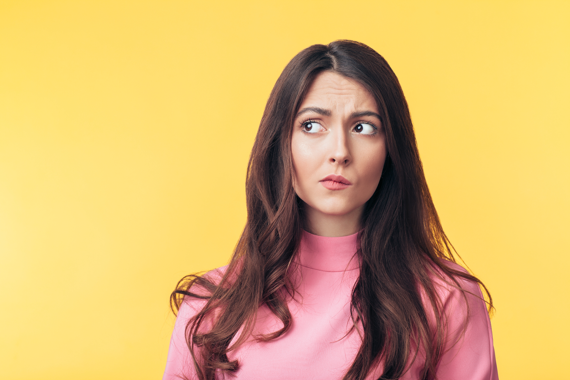 Thoughtful confused woman looking away isolated over yellow back