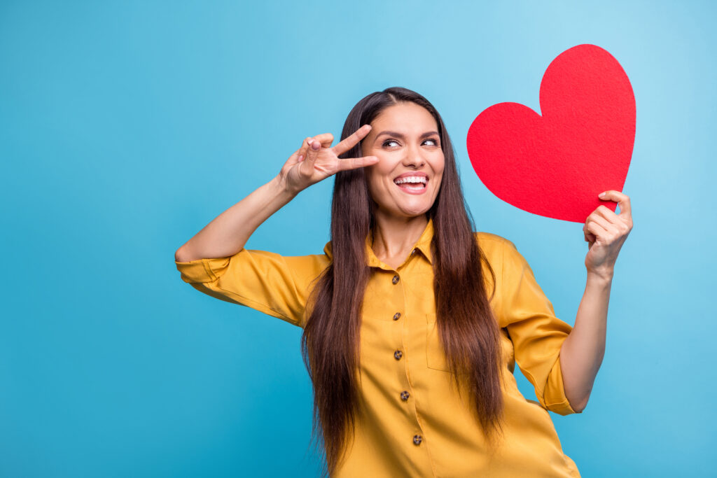 woman holding a heart with two fingers to her face for peace