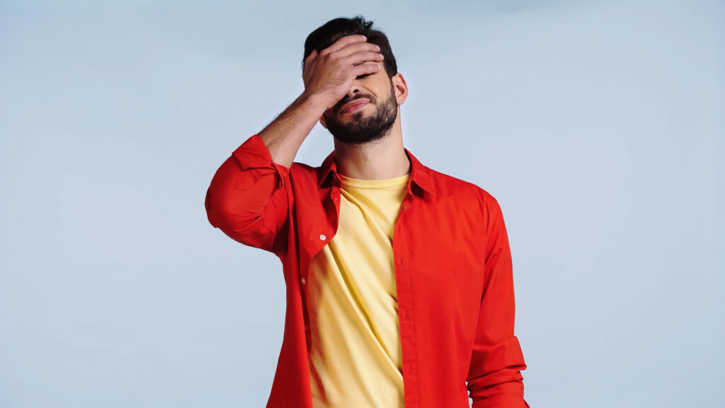 a man wearing a red shirt with his hand over his face in furstration