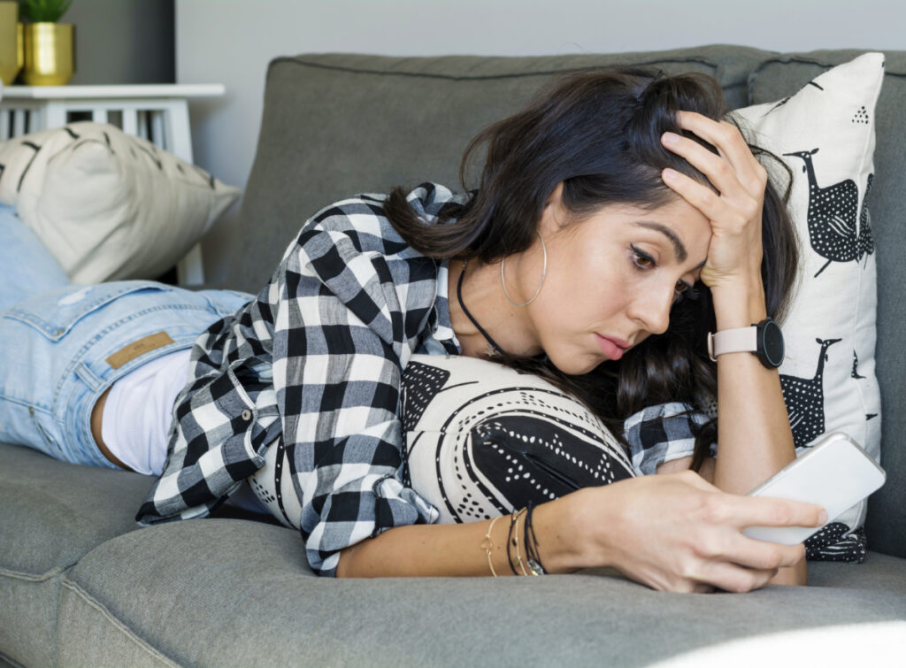 woman laying on the couch looking at her phone wearing a black and white plaid shirt