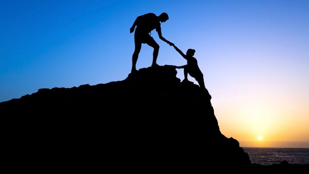 Effort man helping woman up a cliff