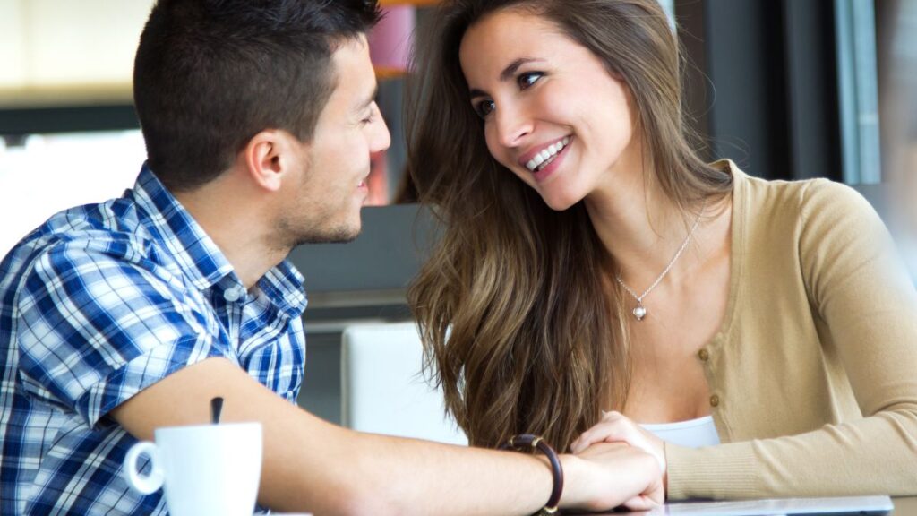 Flirting man and woman sitting and smiling holding hands