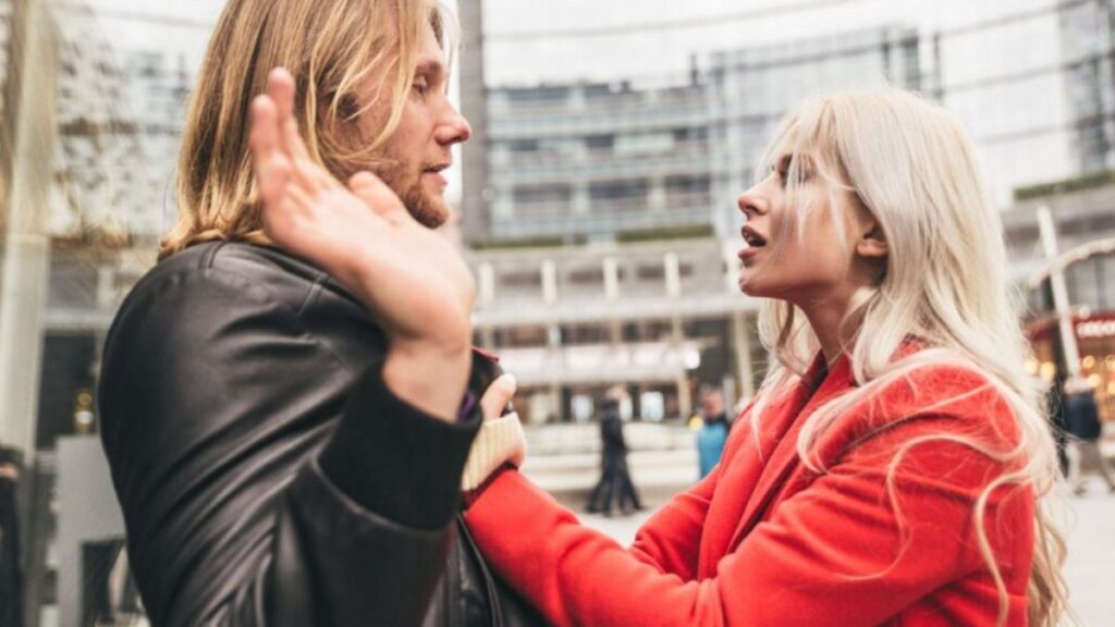 woman grabbing a man by his shirt with his hands up to his side