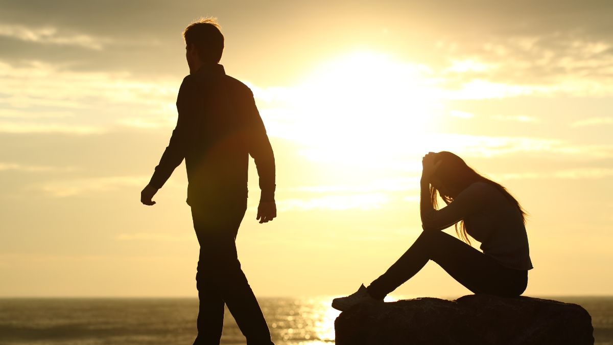 Image of a woman sitting on a rock sad as a man walks away