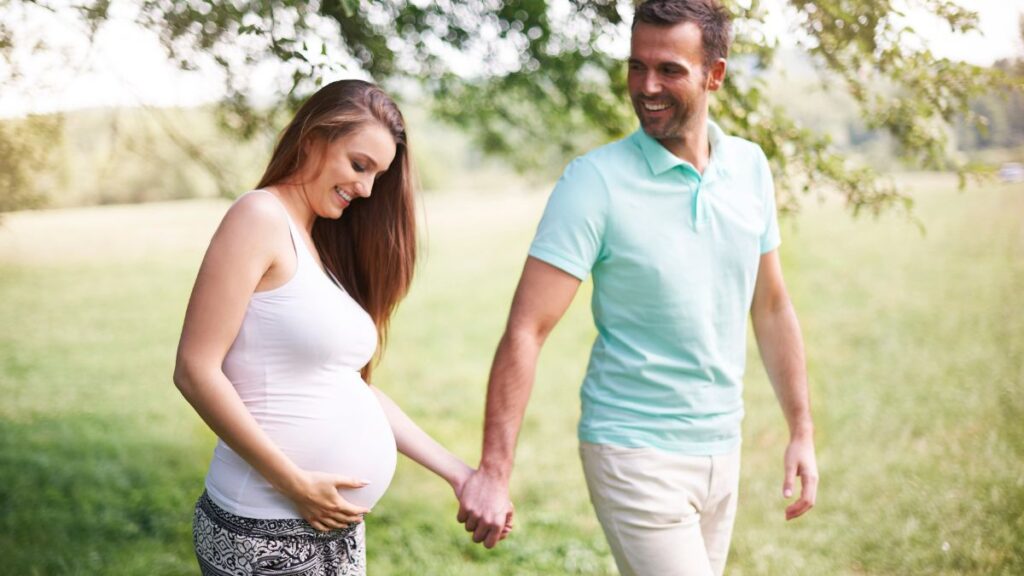 Couple walking outside holding hands and woman looking at pregnant belly