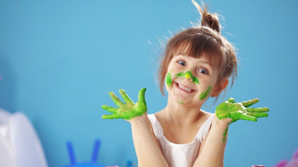 Young girl smiling with green paint on her hands and face.