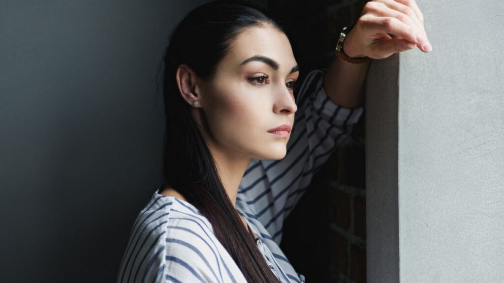 Leave Them Alone: woman looking away with arm up on wall