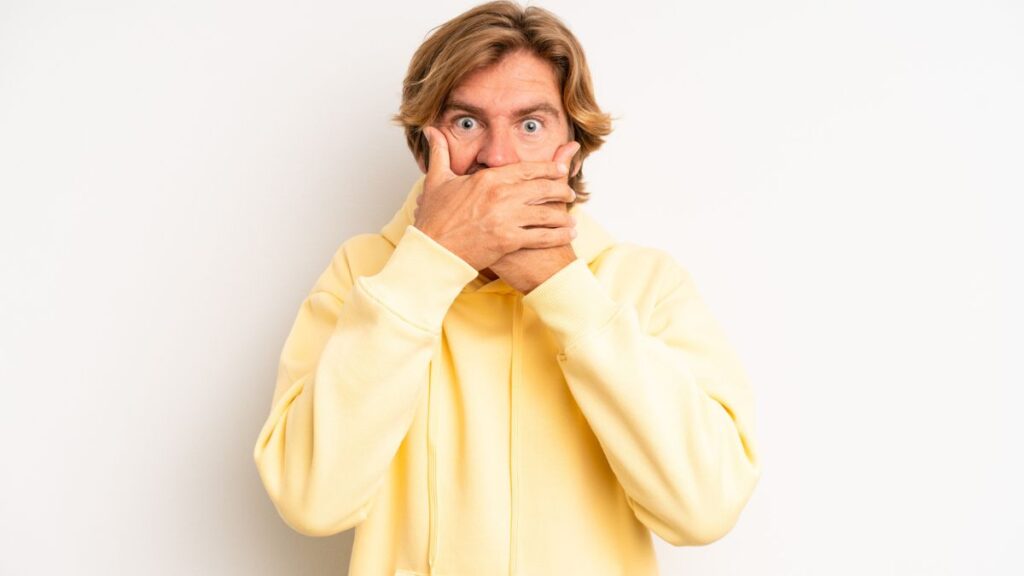 man with a yellow sweater covering his mouth with his hands