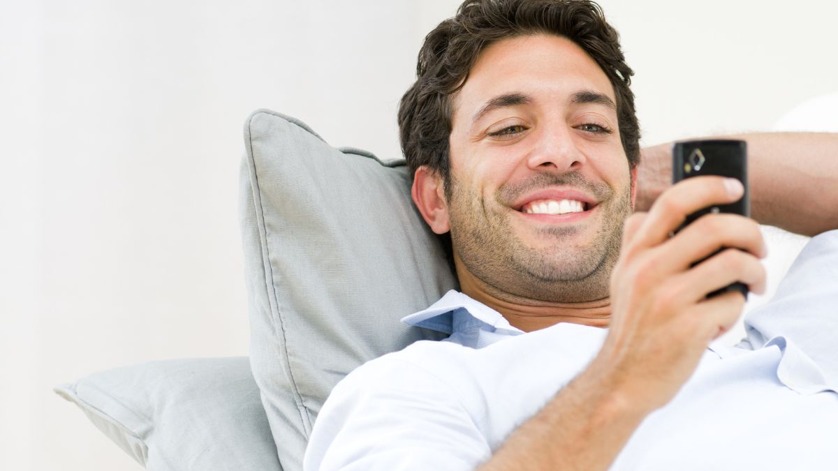 man looking at his phone happily laying down