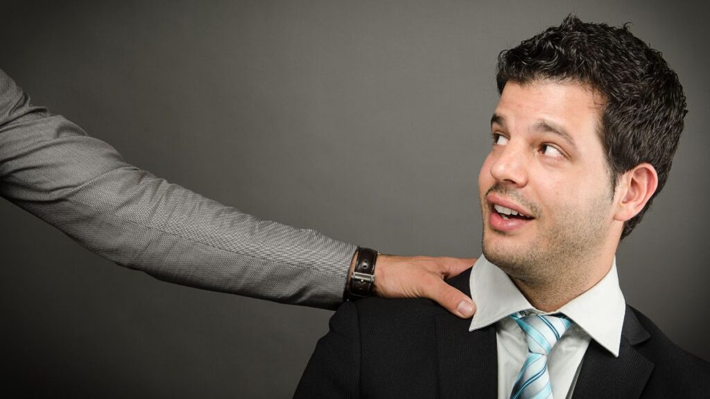 man sitting and looking intimidated with someone else's hand on his shoulder