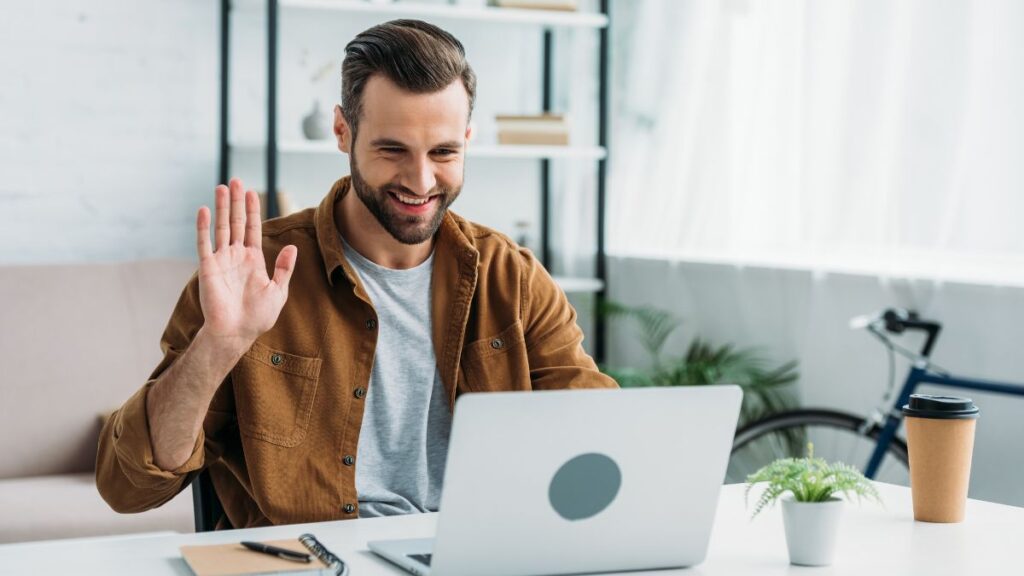 man smiling and waving on his computer