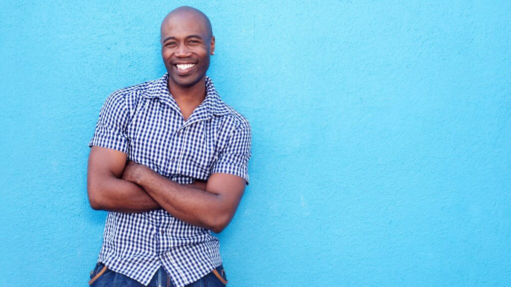 man with arms crossed smiling against a blue wall