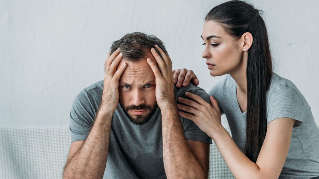 Man with his head in hands while a woman consoles him