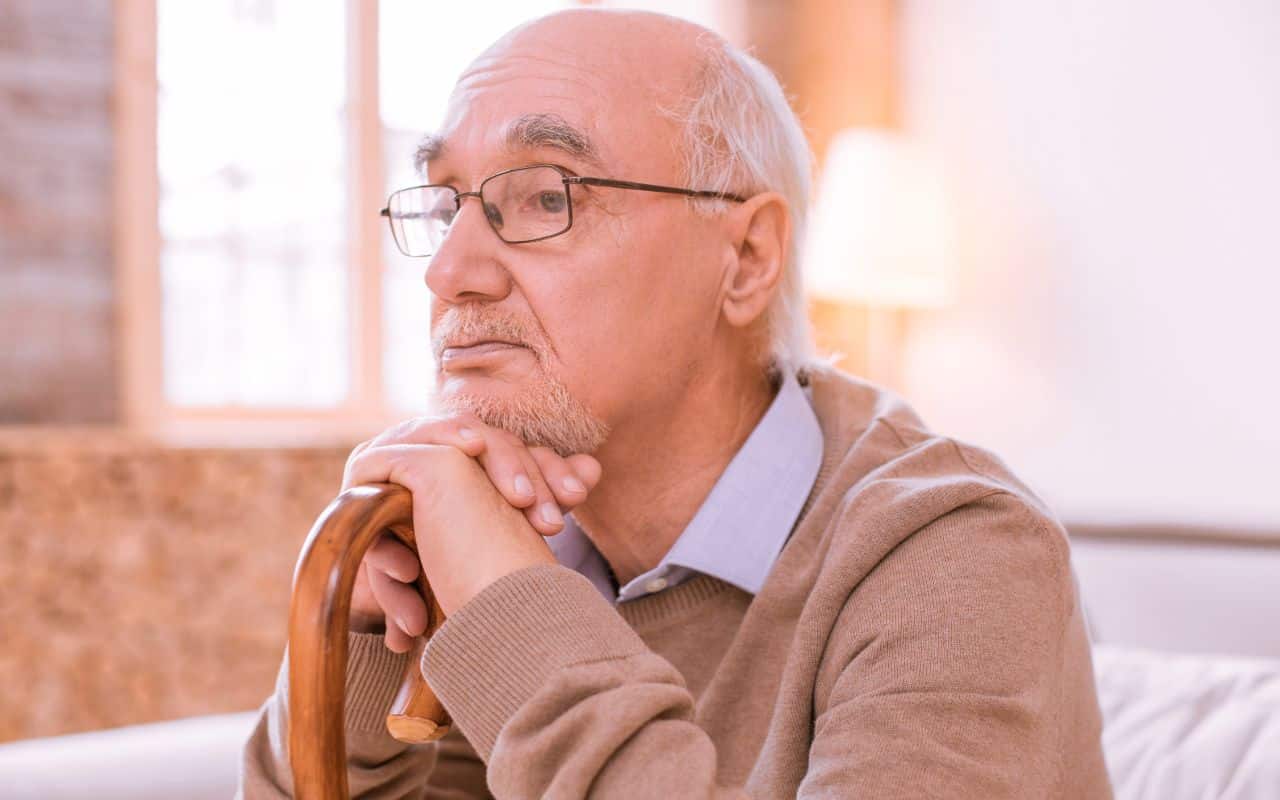 Older man looking sad, chin on his cane