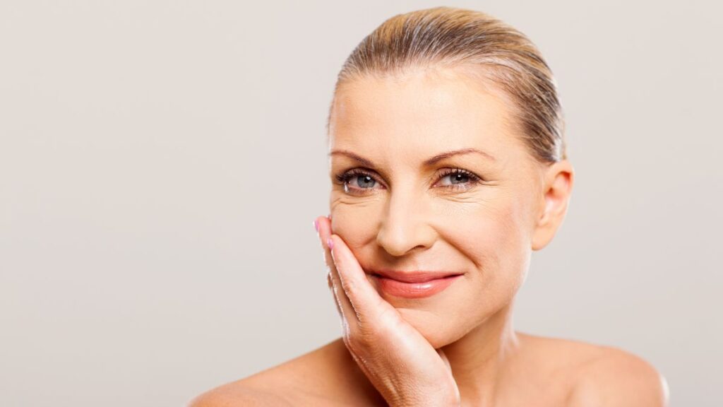 older woman smiling with her hand on her face and hair in a bun