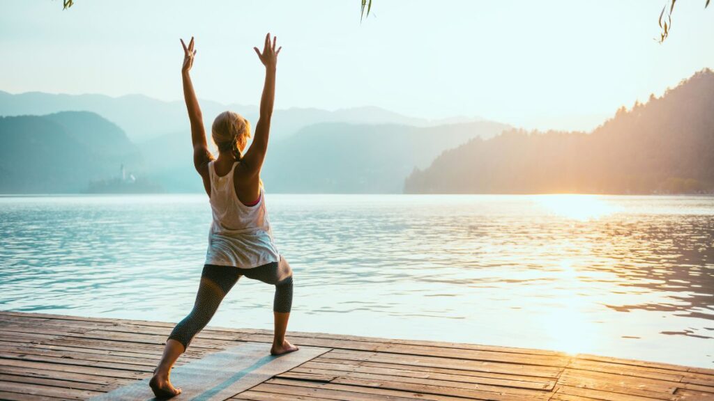 Posture woman in warrior one pose by water on a deck