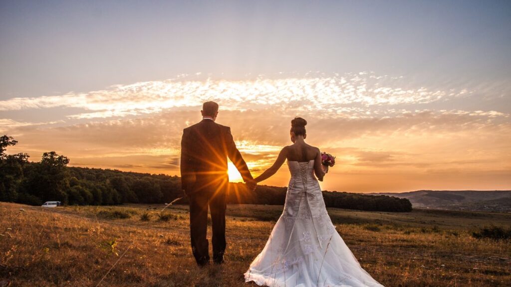 couple holding hands looking at the sunset in wedding outfits