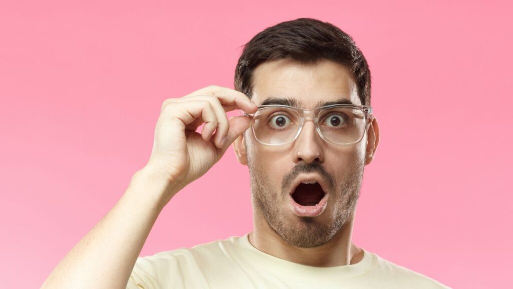 Shocked man holding his glasses - pink background