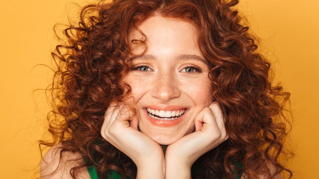 Smile woman smiling with hands under chin curly red hair