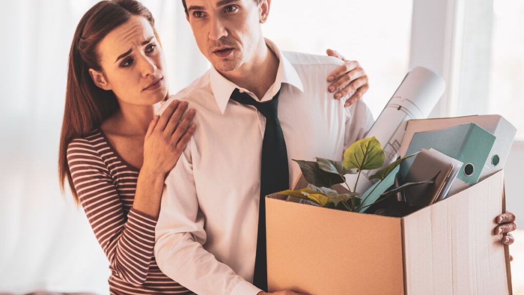 Support Woman giving man a hug from behind. Man holding box of office items upset