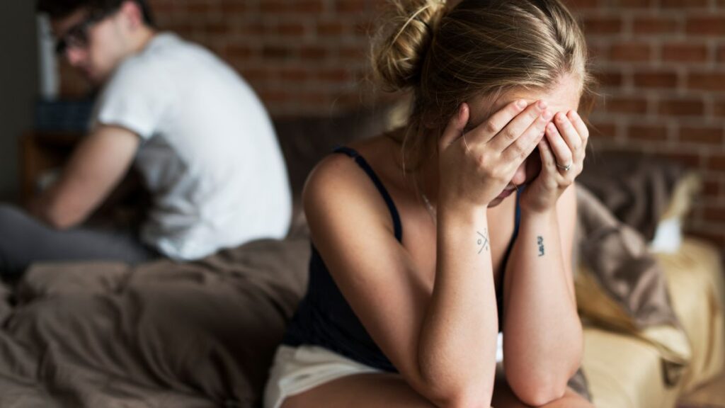 Teasing: woman and man sitting on a bed away from each other woman crying and man looking upset.