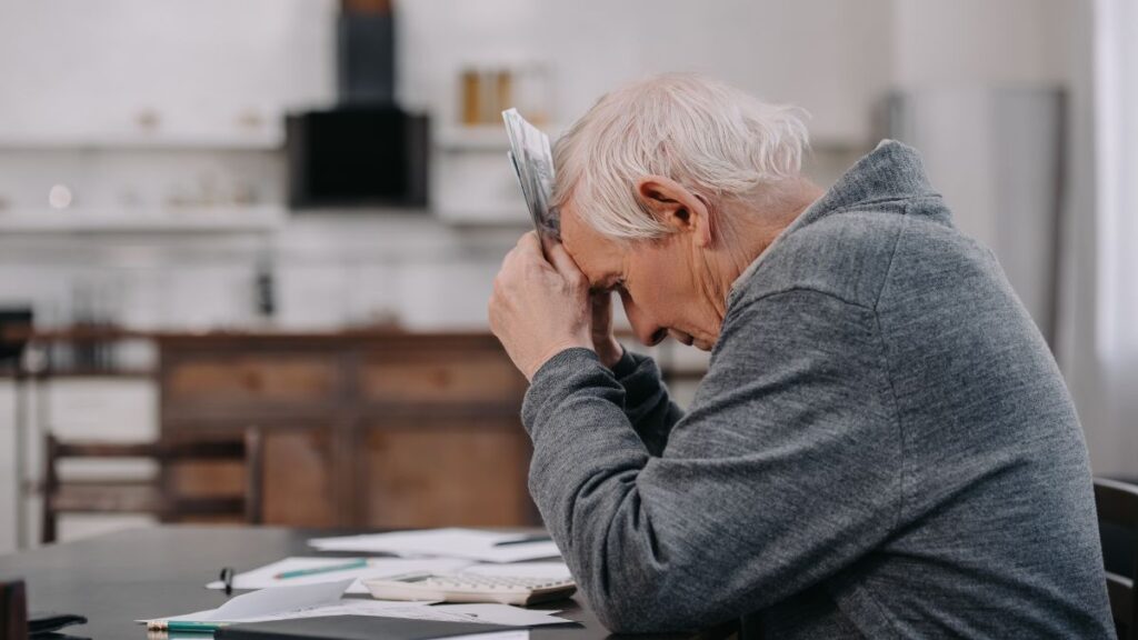 The Household Bills Are Not My Problem:man sitting with his head facing down and holding bills against his head.