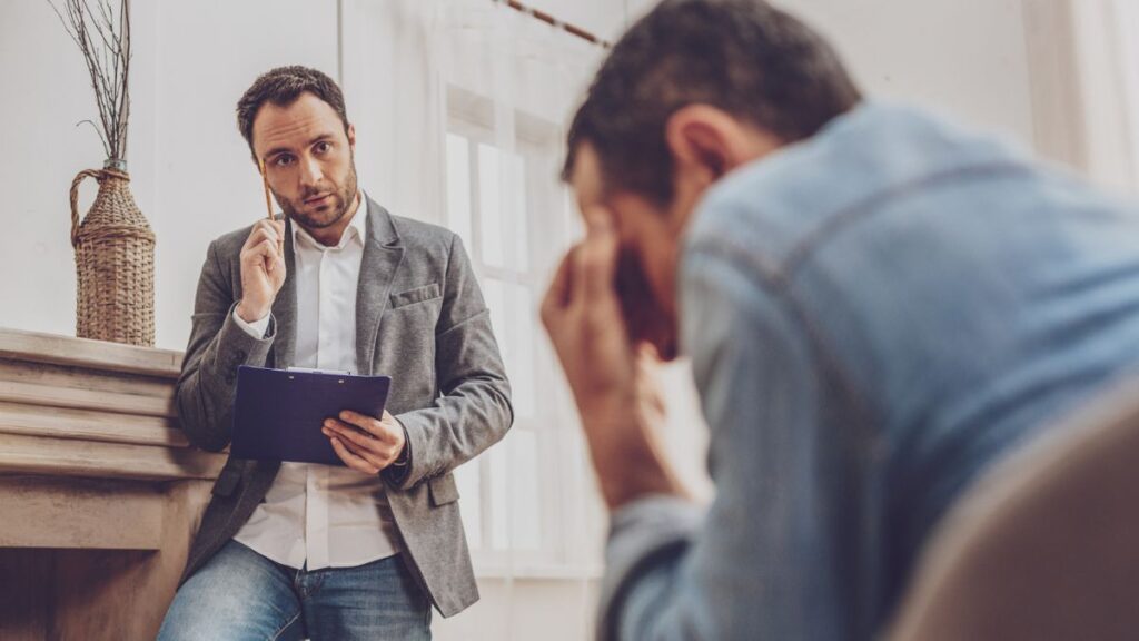 Man sitting talking to a therapist with his hands on his forehead