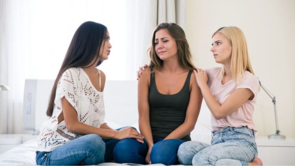 Three women sitting on a bed consoling one girl crying Image credits Depositphotos Vadymvdrobot