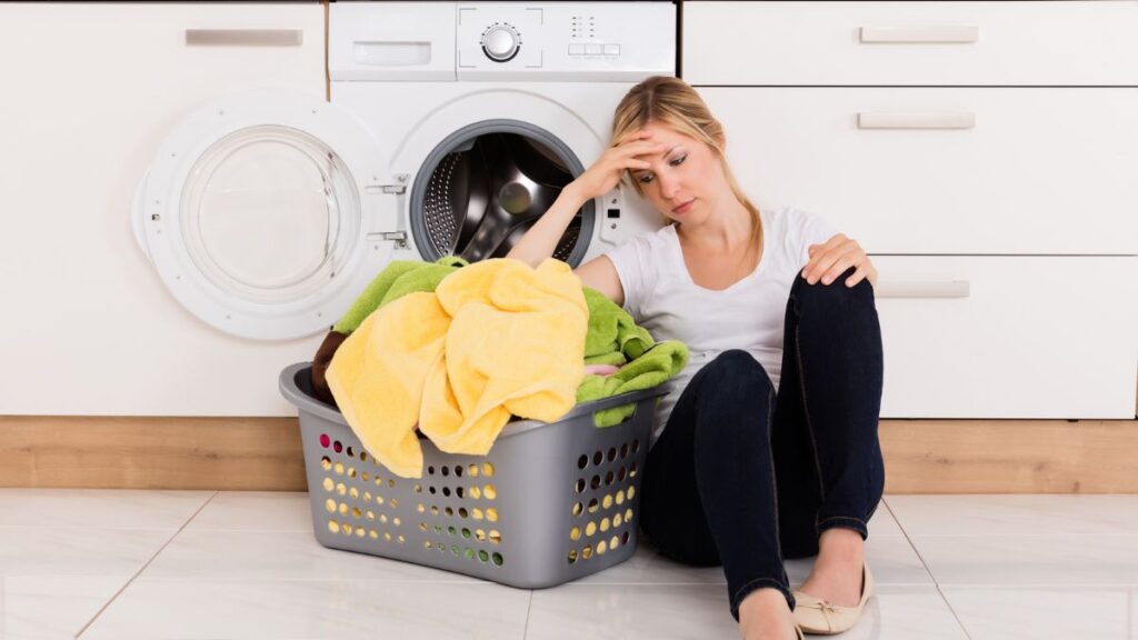 woman sitting on the floor in front of laundry machines with her hand on her head