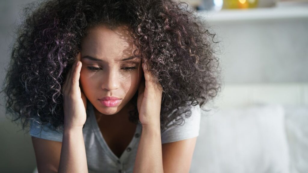 woman holding her head looking upset down at the floor