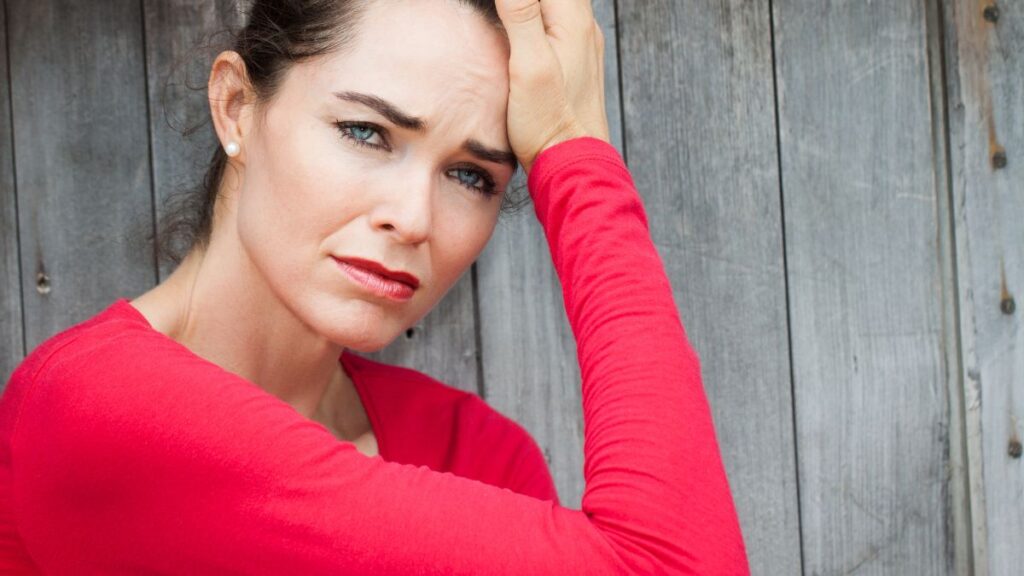 woman looking upset with her hands on her head in a red shirt