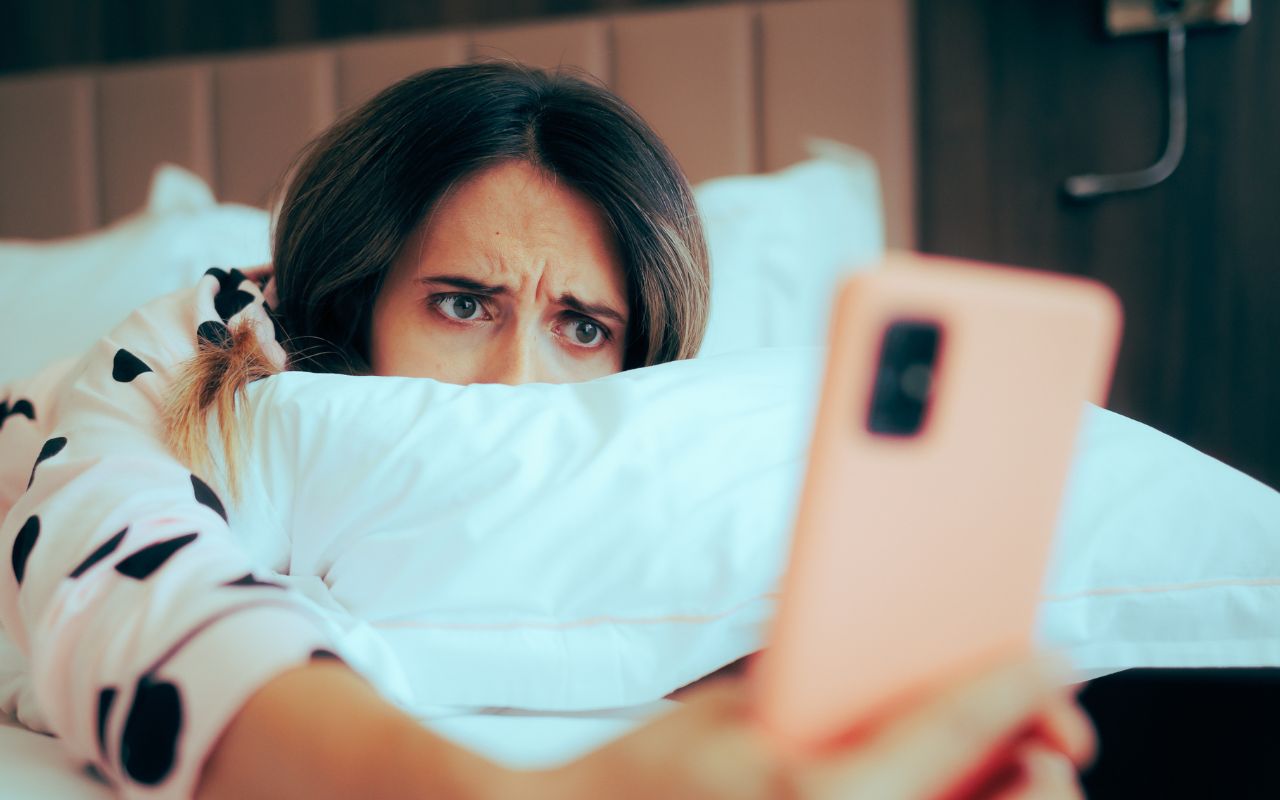 Woman on her phone in bed looking confused