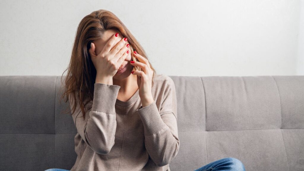 Woman sitting on the couch covering her face on the phone upset